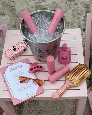 Emi Jay Bamboo Paddle Brush in Lychee Baby. Product is shot on a beach with other Emi Jay products. 