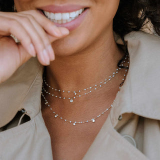 A person wearing a beige jacket and a gigi Clozeau necklace with opal and yellow gold. The necklace features small opal stones with gold accents.