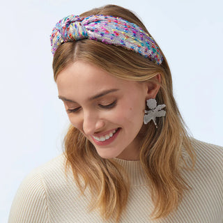 Model is wearing Lele Sadoughi signature knotted headband in silver shimmer yarn with playful confetti detailing.