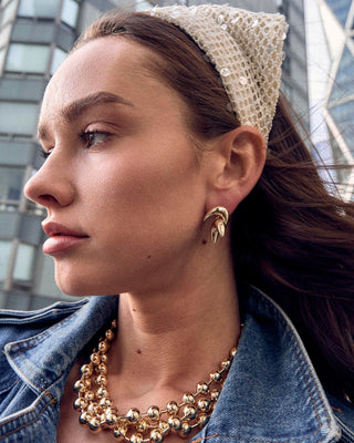 Lele Sadoughi Gold Diana Triple Row Necklace. Model is wearing the product while looking to the left. 