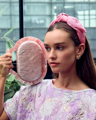 Lele Sadoughi Lilac Molten Heart Button Earrings. Model is wearing the product and is posing with a purse in her hand. 