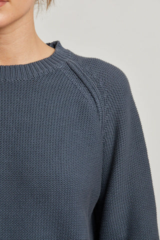 Close-up of a person wearing a textured blue sweater Perfect White Tee Evie Cotton Raglan Crewneck Sweater on a light gray background
