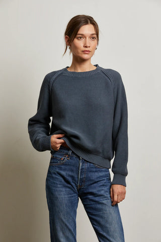 Woman wearing a dark blue sweater Perfect White Tee Evie Cotton Raglan Crewneck Sweater and jeans against a plain background