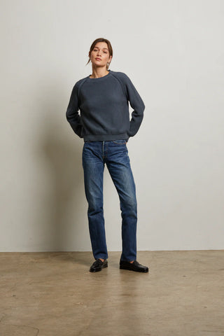 Person wearing a gray sweater Perfect White Tee Evie Cotton Raglan Crewneck Sweater and blue jeans standing against a plain wall.