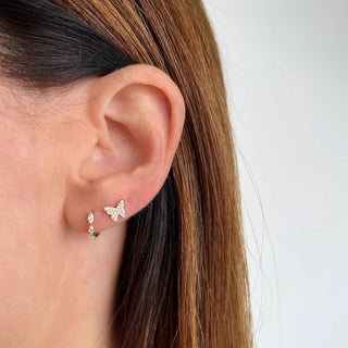 A close-up image of a person wearing a gold butterfly-shaped stud earring with diamond pavé accents. The diamond butterfly stud earring by ef collection