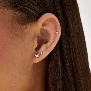 Close-up of an ear wearing two small butterfly earrings by ef collection the baby butterfly stud with a neutral background.